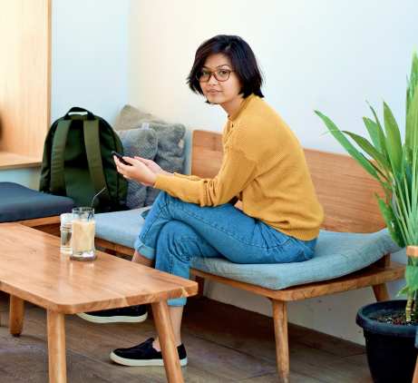 Female student sitting in a coffee shop browsing her phone. 