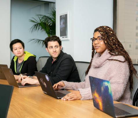 people sitting at a table with their laptop in front of them, looking at one of them