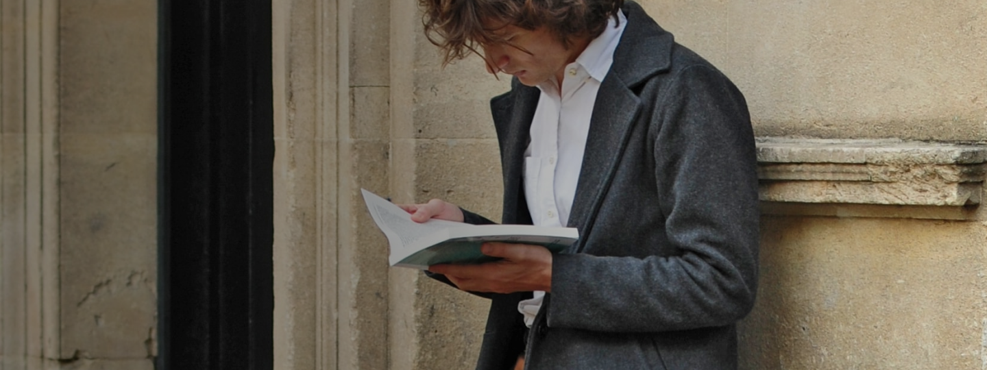 Man standing next to a building reading a book