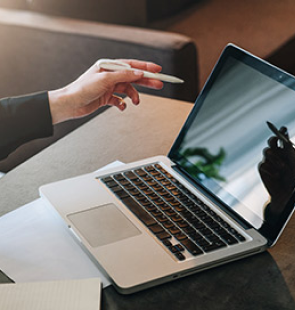 Woman holding a stylus pen and point at a laptop.