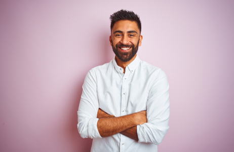 Young man smiling with a whote button down shirt and his arm crossed against his body