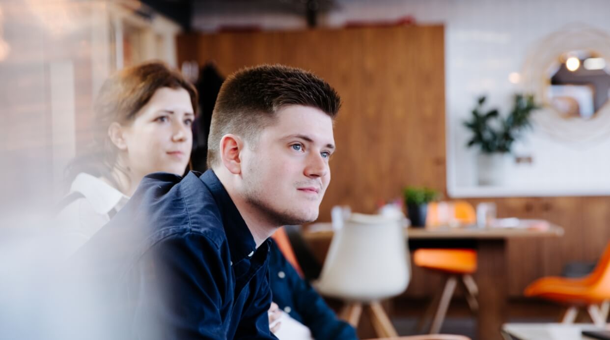 Man standing and women sitting in their chairs listening attentively. 