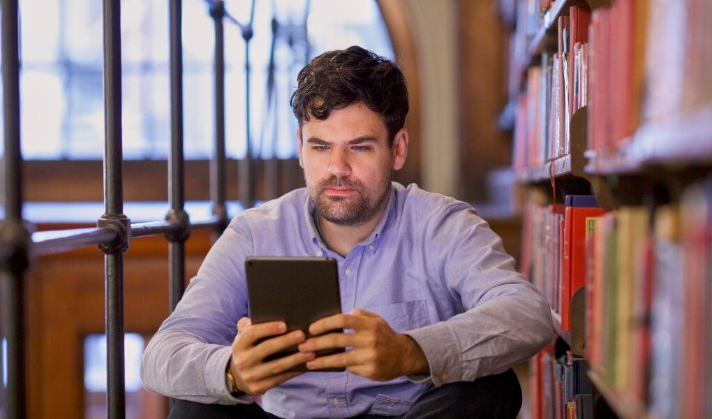 a man in a library looking at a tablet