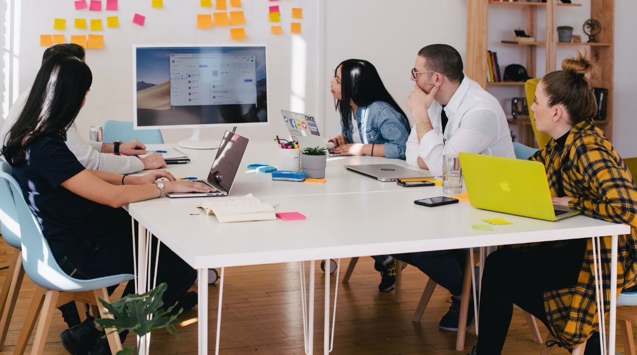 Group of professionals sitting at an office desk looking at a monitor. 