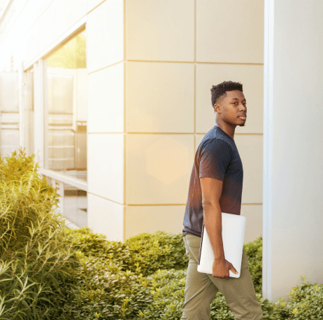 Young man holding his laptop walking into university building.