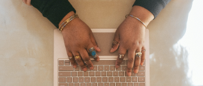 Hands decorated in jewelery and typing on a keyboard. 