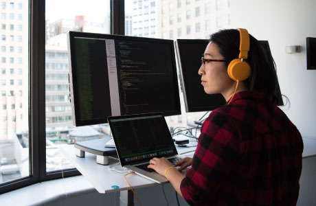 Woman working on a laptop in front of 2 big monitors
