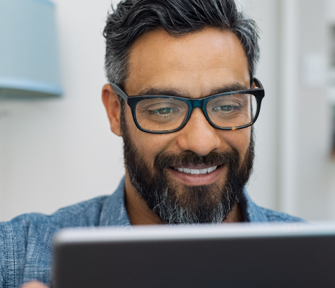 Man with glasses smiling while looking at a screen