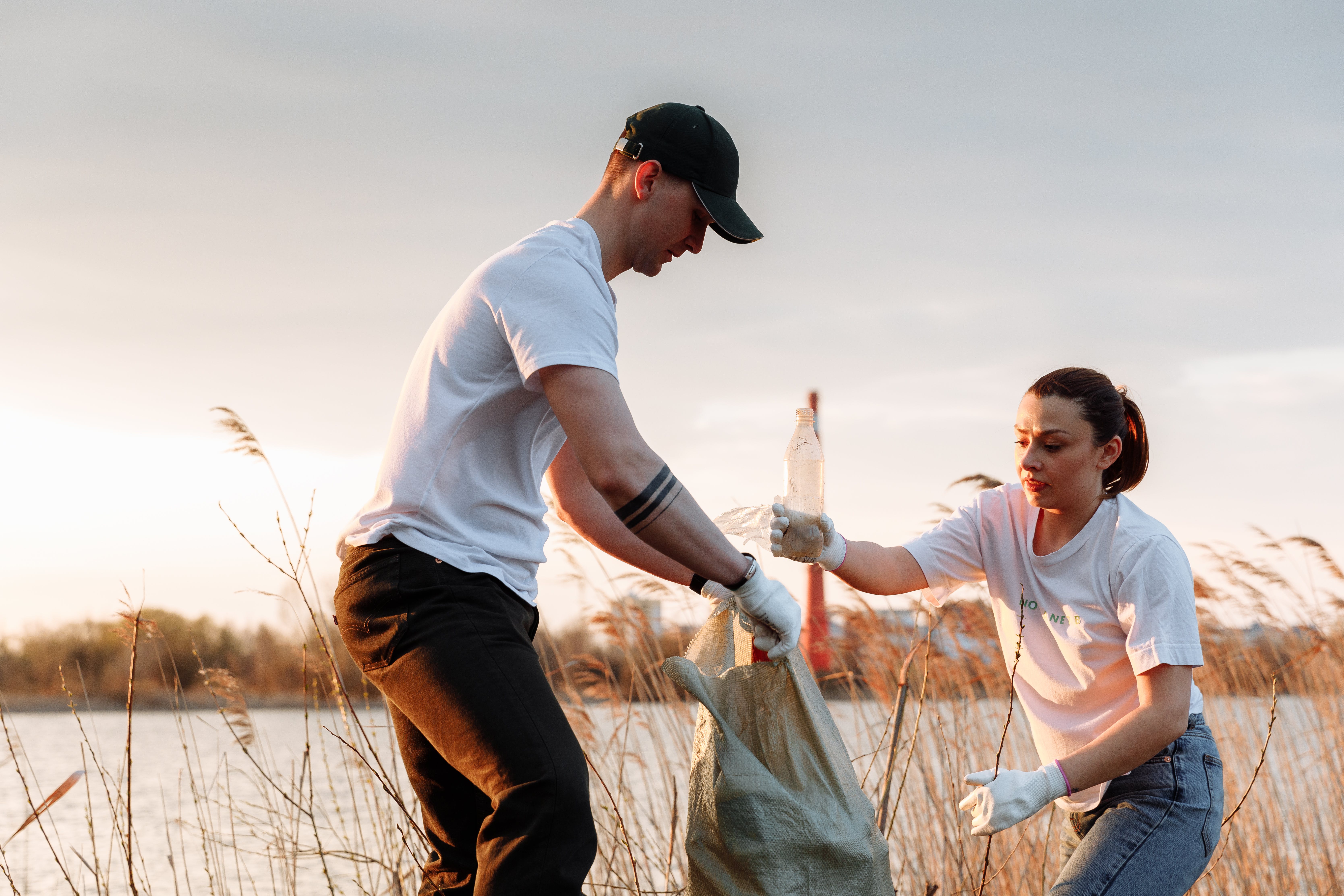 Man holding a trash bag while women is placing trash in it.